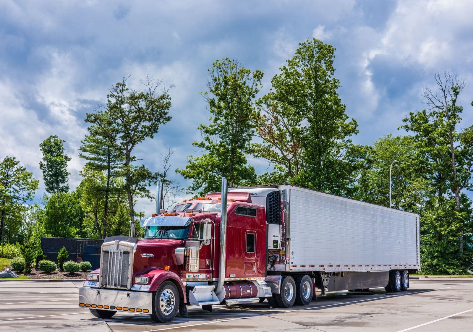 A red semi truck parked under trees, the first truck of a new authority